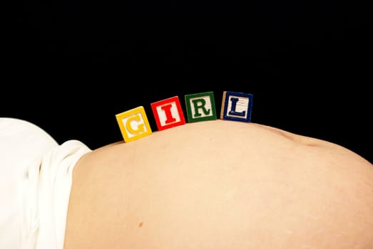 An expecting mother rests some baby blocks on her pregnant belly that spell out the word girl.