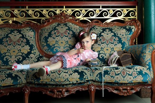 A girl plays with her ​​mother's jewelry lying on the couch.