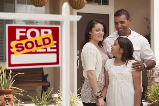 Hispanic Mother, Father and Daughter in Front of Their New Home with Sold Home For Sale Real Estate Sign.