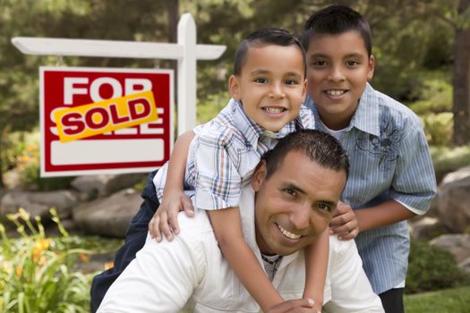 Hispanic Father and Sons in Front of a Sold Home For Sale Real Estate Sign.