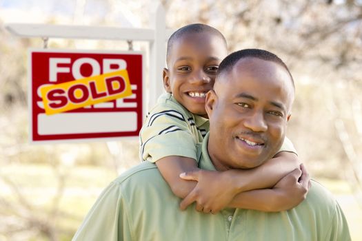 Happy African American Father and Son in Front of Sold Real Estate Sign.