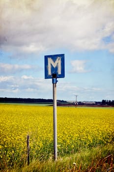 Street sign in the countryside by a rape field, textured.