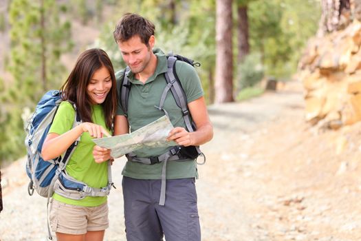hiking - hikers looking at map. Couple or friends navigating together smiling happy during camping travel hike outdoors in forest. Young mixed race Asian / Caucasian woman and Caucasian man.