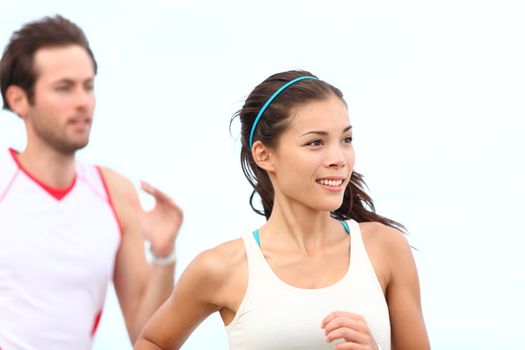 Runners jogging. Young couple running outside training for marathon. Asian woman sport model smiling happy with caucasian male runner in background.