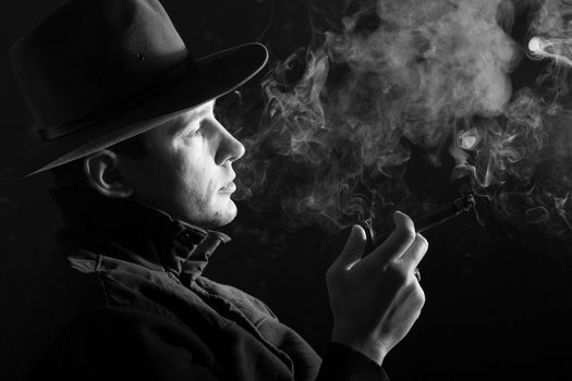 A man in a hat smoking a cigar in puffs of smoke