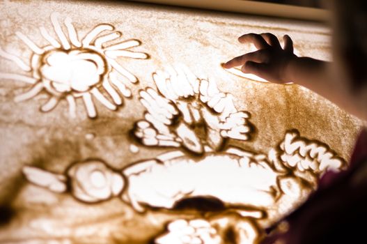 Child paint an illustration with sand on light table by finger