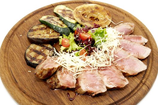 meat roasted on a grill with vegetables on a wooden plate