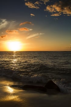 Sunset over a calm pacific ocean on rocks a beach being pounded by waves