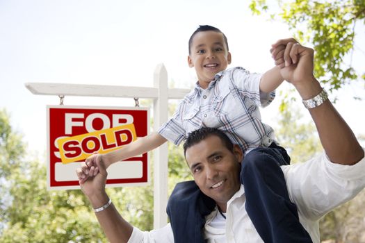 Excited Hispanic Father and Son in Front of Sold For Sale Real Estate Sign.