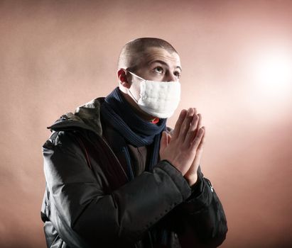 A praying man in a protective mask on brown background