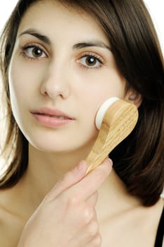 An image of a young woman cleaning her face with a brush