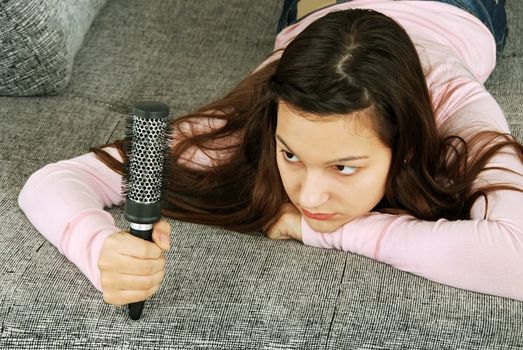 caucasian teenage girl lying on stomach looking at her hairbrush, thinking about her hairs