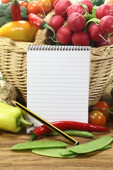 Ruled shopping list with fresh vegetables in a basket on a wooden ground