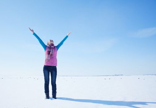 Teen girl staying with raised hands against blue sky