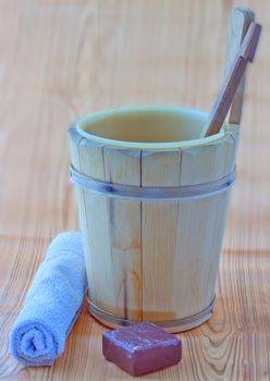 Wooden bucket, brown soap and towel over wooden background