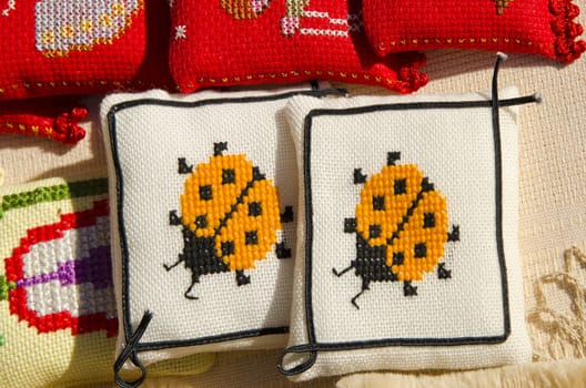 Handmade sewing needlework fancywork with pillows embroided ladybird sold in outdoor street fair market.