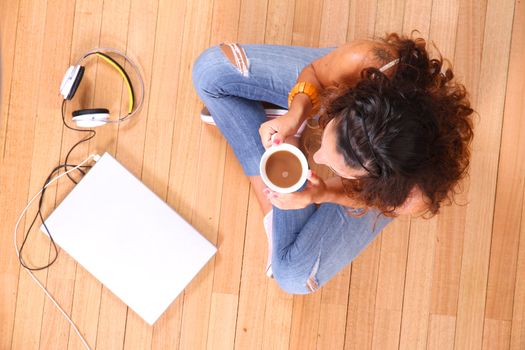 A girl sitting on the floor with a Laptop and some coffee.