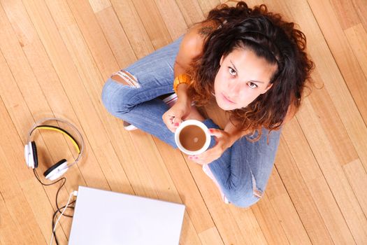 A girl sitting on the floor with a Laptop and some coffee.