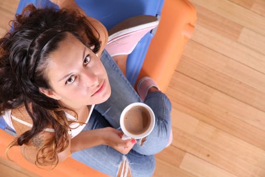 A young woman sitting on a stack of suitcases while drinking coffee and waiting for the departure to vacations.