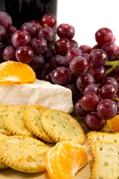 Picture of some grapes brie and some clementins with a bottle of red wine in the background