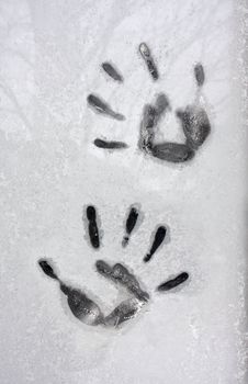 impressions of hands are left on a frost covered window pane