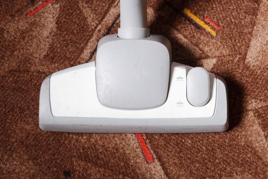 Close-up of a vacuum cleaner picking up dust and dirt from a brown carpet