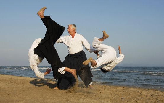 Three adults are training in Aikido on the beach