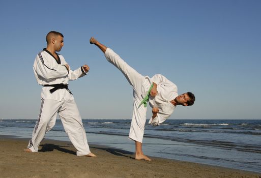 two men are training of taekwondo on the beach