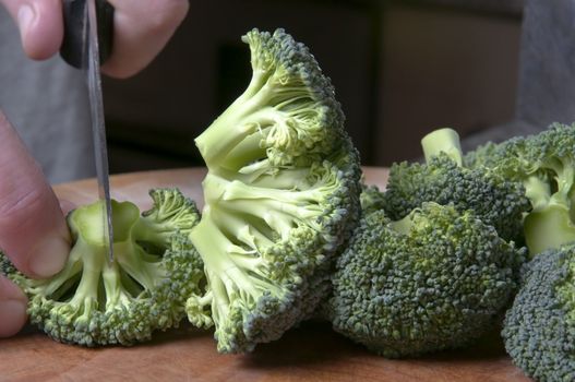 Close up of male hand, cutting broccoli over a wooden chopping board in a kitchen setting.