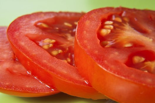 Macro shot of three tomato slices on a green surface.  Skin and seeds visible.