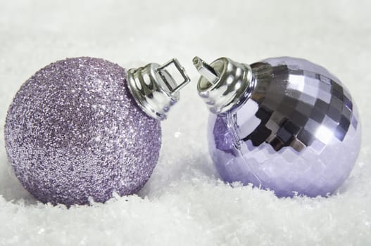 Close up of two mauve Christmas baubles on fake snow, leaning towards eachother as though in love or about to kiss.  One glittery, the other shiny and faceted. 