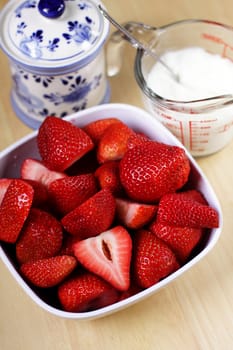Strawberries in white bowl on the kitchen table with sugar pot and a glass of cream