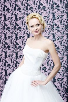 20s yeared blonde bride posing in white wedding dress. She is slightly smiling