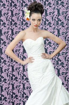 Young adult bride in white wedding dress posing over magenta wall. Her hair decorated with lily flowers