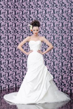 Young adult bride in white wedding dress posing over magenta wall. Her hair decorated with lily flowers