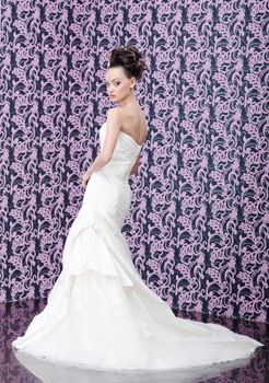 Young adult bride in white wedding dress posing over magenta wall. She is looking in camera over the shoulder
