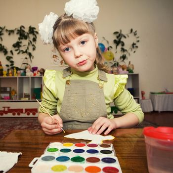 A little girl sitting at the table and painting gouache in a kindergarten