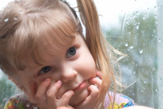 A girl looking through the glass covered with raindrops