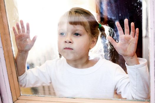 Portrait of a young girl  stands outside the window.