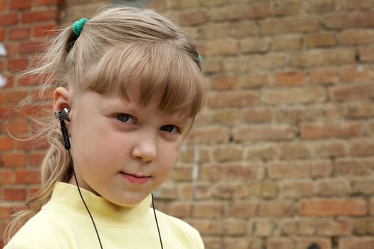 The young girl listens to music on a background of a brick wall