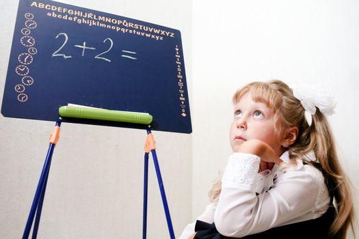 An image of Little girl sitting near chalkboard.