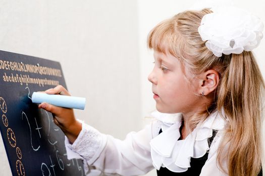 An image of Little girl writing on blackboard.