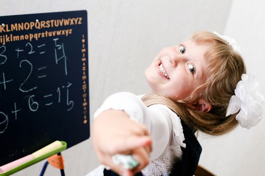 An image of Little girl standing near chalkboard. 