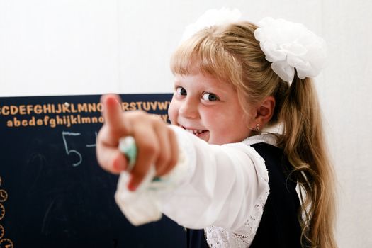 Little girl standing near chalkboard. Writing on it.