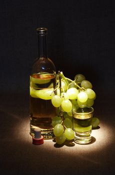 Bunch of grapes near bottle of white wine and wineglass on dark background