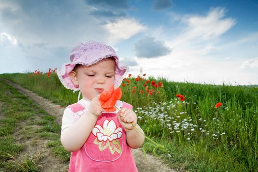 Baby-girl with red poppy on the lane amongst green field