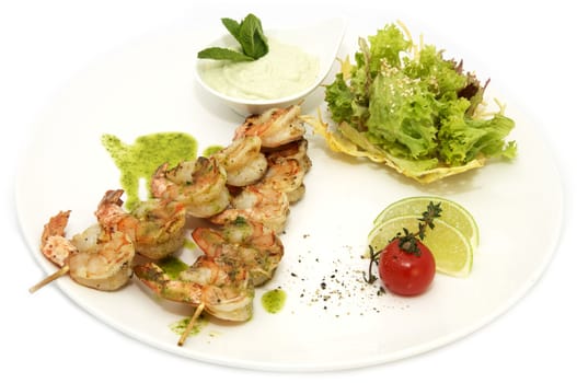 skewers of shrimp on a white plate with greens