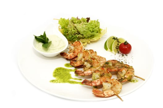 skewers of shrimp on a white plate with vegetables and lemon