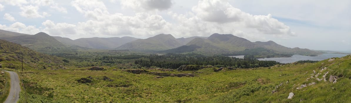 Panoramic photo of Irish landscape: hills, ocean and sky with clouds. This photo is made attaching together various photos.