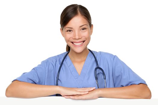 Nurse leaning on sign edge smiling happy. Young woman doctor, nurse or medical professional smiling happy isolated on white background. Multiracial Chinese Asian / Caucasian model in blue scrubs.